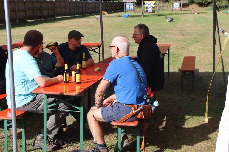 Teilnehmer sitzen an Biertischen vor dem Vereinsgelände in der Sonne