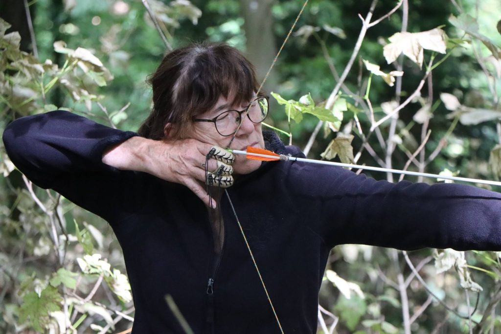 Bogenschützin mit Brille spannt den Bogen, Nahaufnahme im Wald