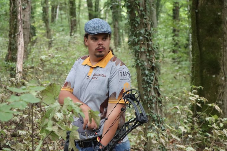 Bogenschütze mit Schiebermütze und Compoundbogen steht im Wald