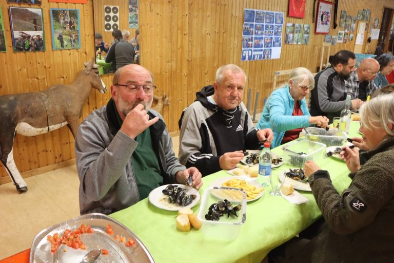 Teilnehmer essen Muscheln an einer Tafel im Vereinshaus, im Hintergrund ein ausgestopftes Reh
