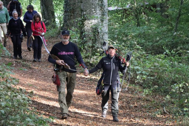 Zwei Bogenschützen mit Bögen gehen voraus, dahinter folgt ihre Gruppe durch den Wald
