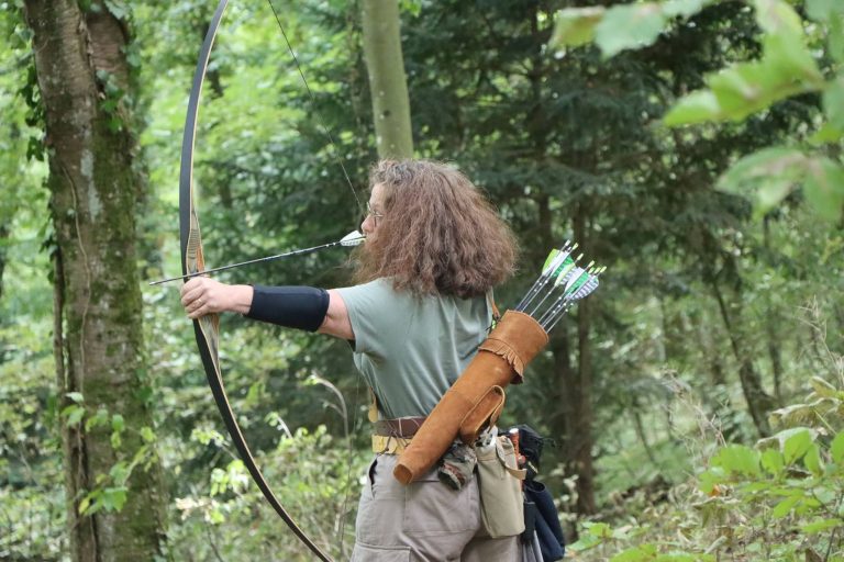 Bogenschützin mit Locken und Lederköcher spannt einen Langbogen im Wald