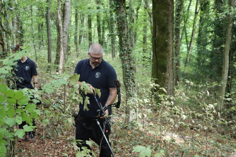 Bogenschütze in dunkler Kleidung geht mit seinem Bogen durch den Wald