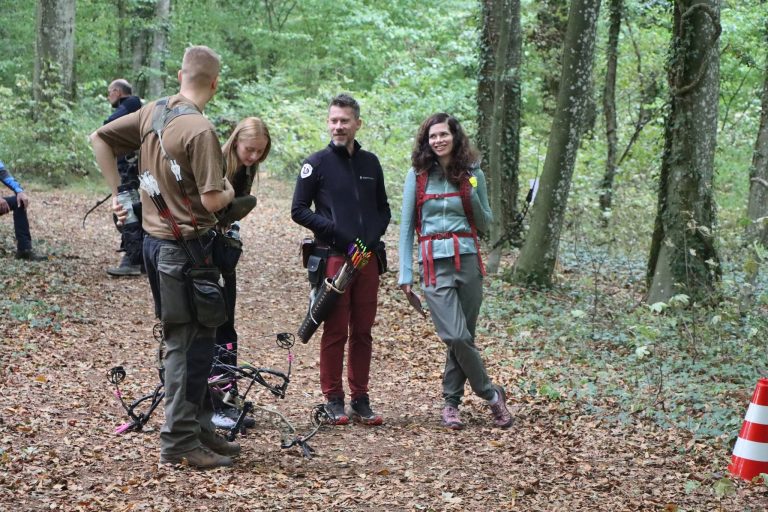 Mehrere Bogenschützen warten auf einem laubbedeckten Waldweg
