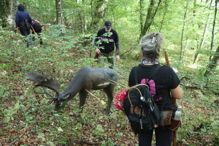 Bogenschützin mit Rucksack steht vor einem 3D-Hirschziel am Waldhang