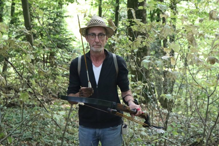 Bogenschütze mit Strohhut hält seinen Bogen im Wald