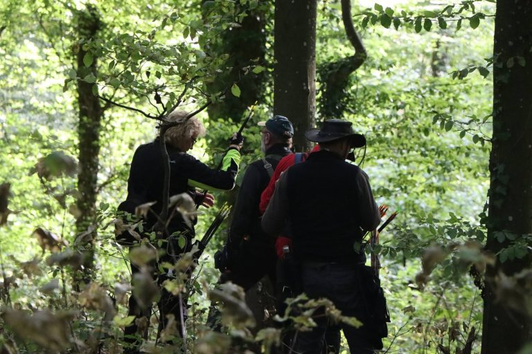 Silhouetten von Bogenschützen mit Hüten im Gegenlicht zwischen Bäumen