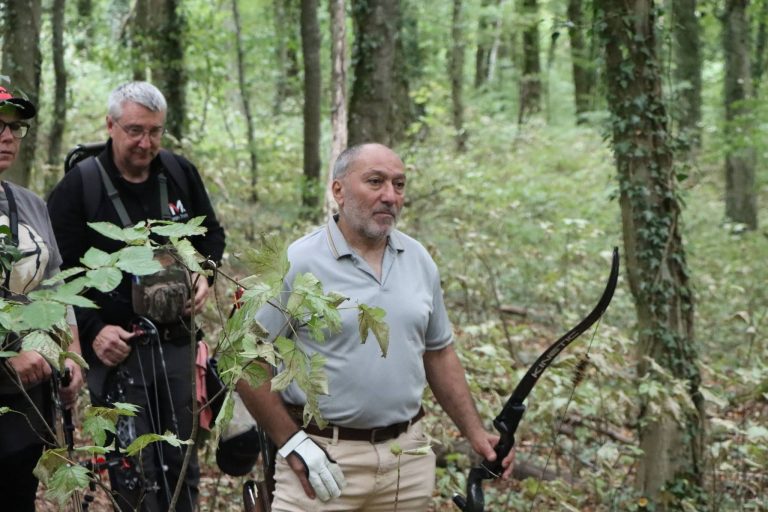 Bogenschütze mit weißen Handschuhen und Recurvebogen wartet mit seiner Gruppe im Wald
