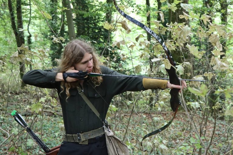 Langhaariger Bogenschütze in grüner Kleidung spannt einen traditionellen Bogen