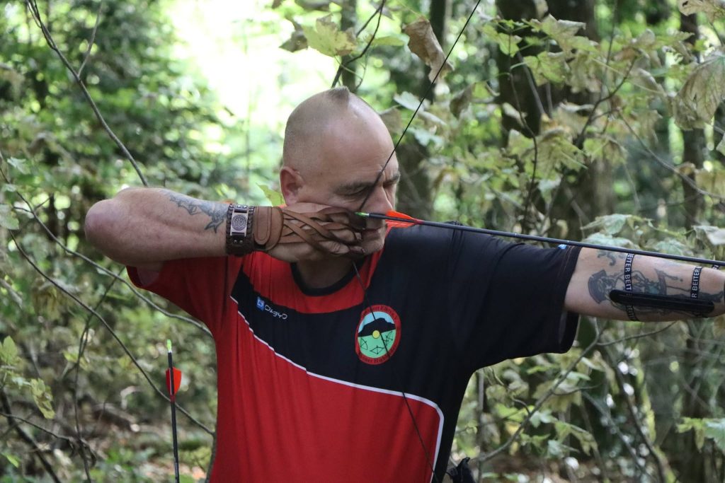 Bogenschütze mit Glatze und rot-schwarzem Trikot spannt den Bogen, Nahaufnahme