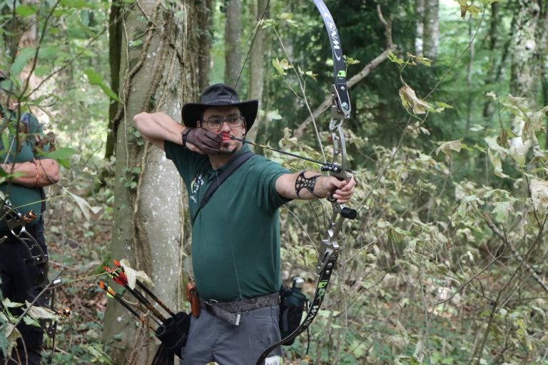 Bogenschütze mit Hut und grünem T-Shirt spannt einen Recurvebogen im Wald