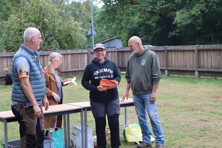 Vier Personen bei der Siegerehrung auf der Wiese, eine Frau hält einen orangefarbenen Preis