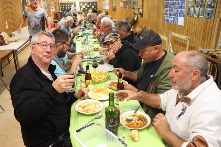 Männer stoßen an einer langen Tafel mit Wein an, vor ihnen Teller mit Essen