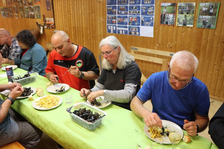 Teilnehmer essen Muscheln mit Pommes an einer langen Tafel im Vereinshaus
