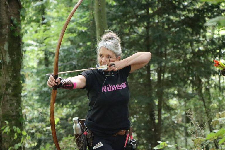 Bogenschützin mit Haarknoten spannt einen Langbogen im Wald