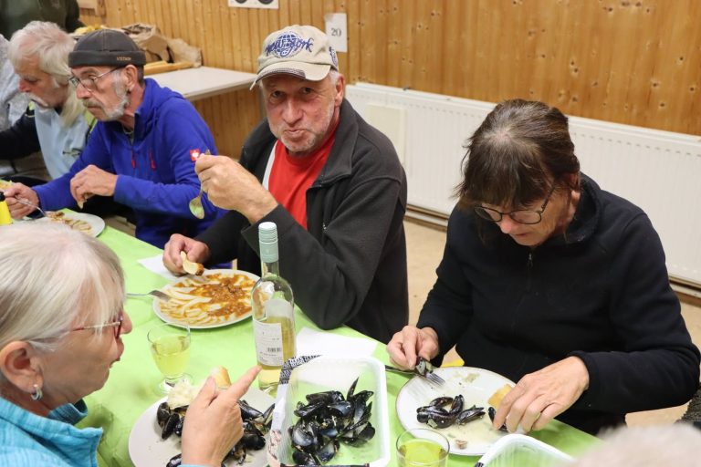 Teilnehmer essen Muscheln und trinken Wein an einer Tafel im Vereinshaus