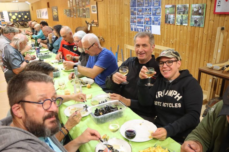 Gut gelaunte Teilnehmer beim Essen an langen Tischen im Vereinshaus, einige heben ihr Glas
