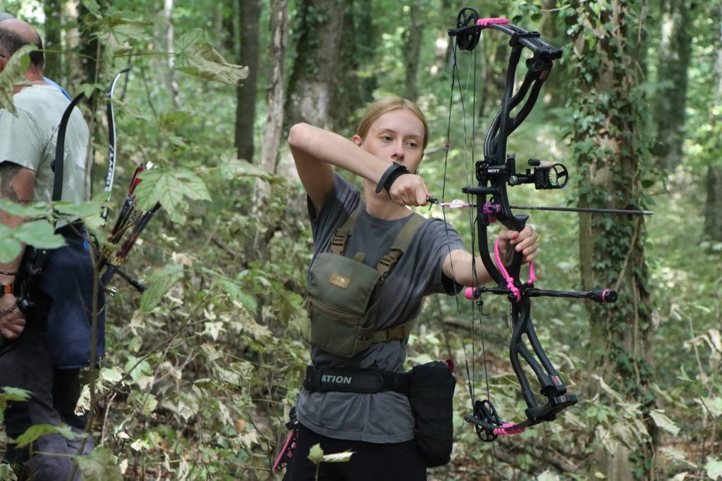 Junge Bogenschützin spannt einen pinkfarbenen Compoundbogen im Wald