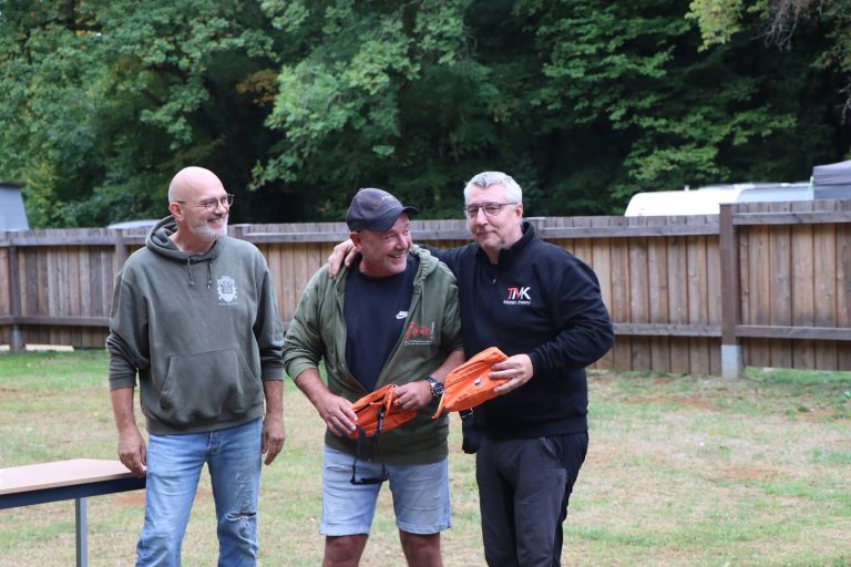 Drei Männer bei der Siegerehrung auf der Wiese, einer hält orangefarbene Preise