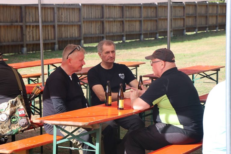 Drei Männer sitzen am Biertisch vor dem Vereinshaus und unterhalten sich