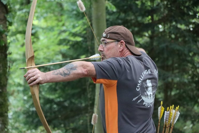 Bogenschütze mit Kappe und Tattoo spannt einen Langbogen aus Holz