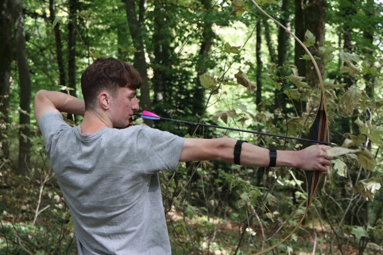 Junger Bogenschütze in grauem T-Shirt spannt einen Recurvebogen im Wald