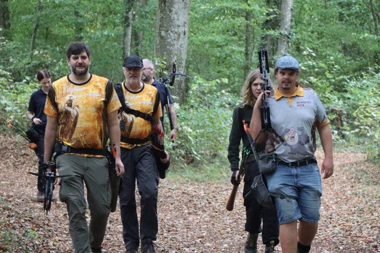 Gruppe von Bogenschützen in gelb-schwarzen Trikots geht über einen Waldweg