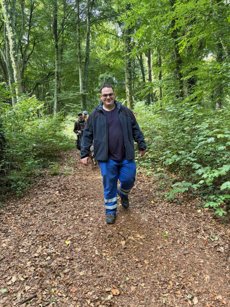 Mann in dunkler Jacke geht lächelnd einen Waldweg entlang