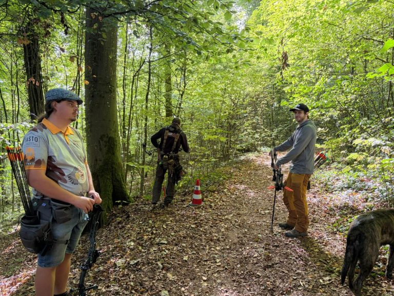 Drei Bogenschützen und ein Hund auf einem Waldweg