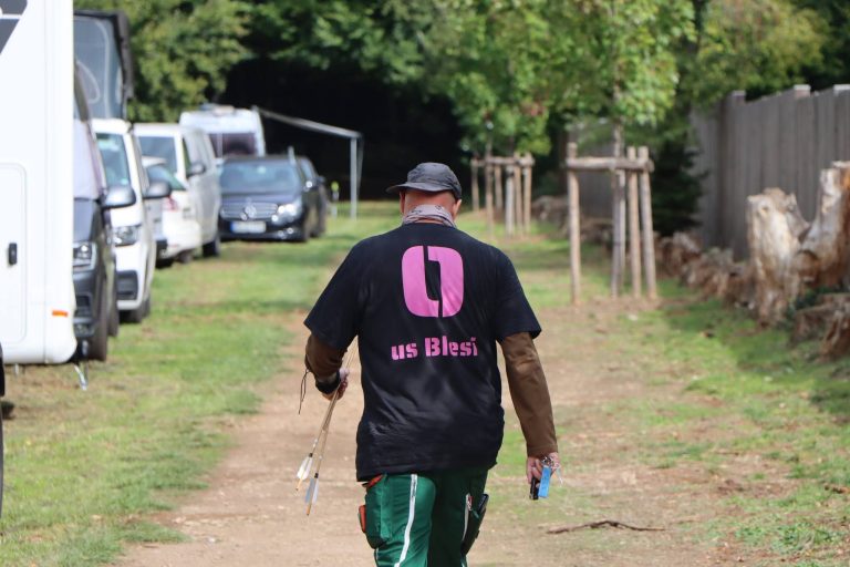 Mann in schwarzem T-Shirt geht einen Weg entlang an abgestellten Wohnmobilen vorbei