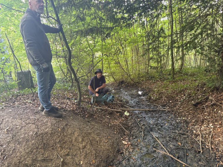 Zwei Männer an einem feuchten Waldgraben, einer sitzt am Boden