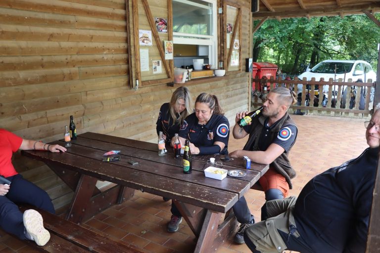 Teilnehmer sitzen mit Getränken am Holztisch auf der Terrasse des Vereinshauses