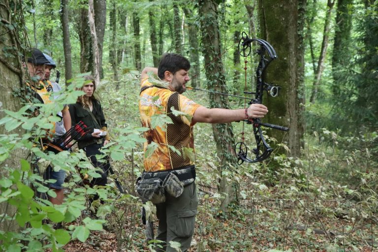 Bogenschütze im gelb-schwarzen Trikot zielt mit einem Compoundbogen im Wald