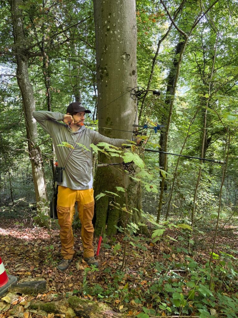 Bogenschütze mit gelber Hose lehnt mit seinem Bogen an einem Baum