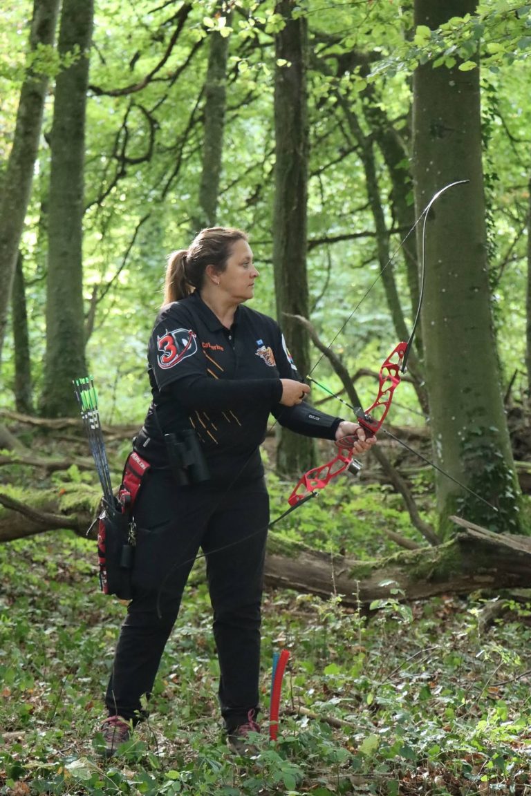 Bogenschützin mit Zopf und rotem Recurvebogen steht im Wald