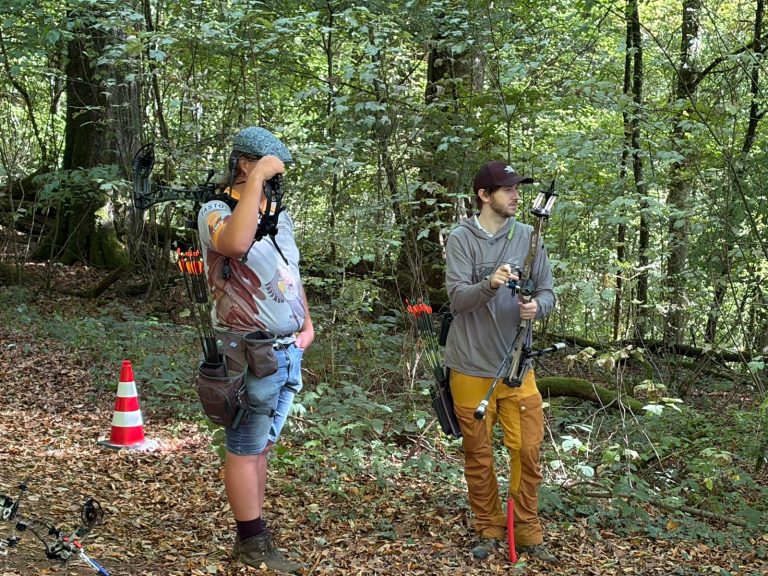 Zwei junge Bogenschützen mit Bögen stehen an einer Station im Wald