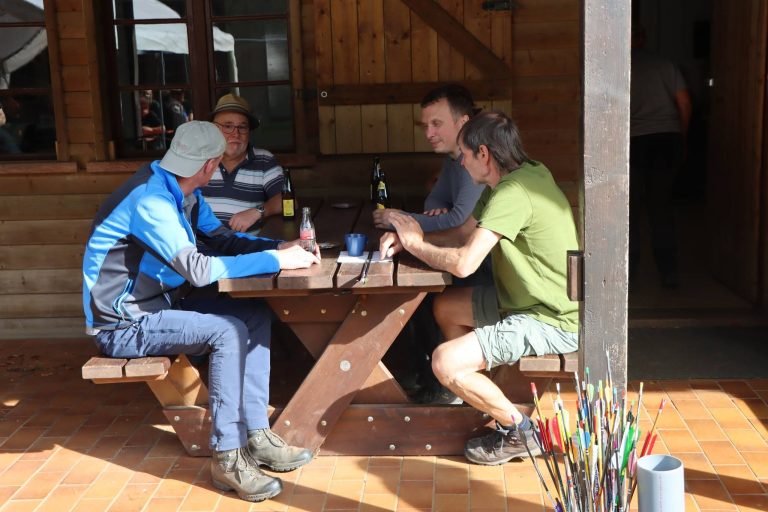 Drei Männer sitzen am Holztisch auf der Terrasse, davor ein Köcher mit Pfeilen