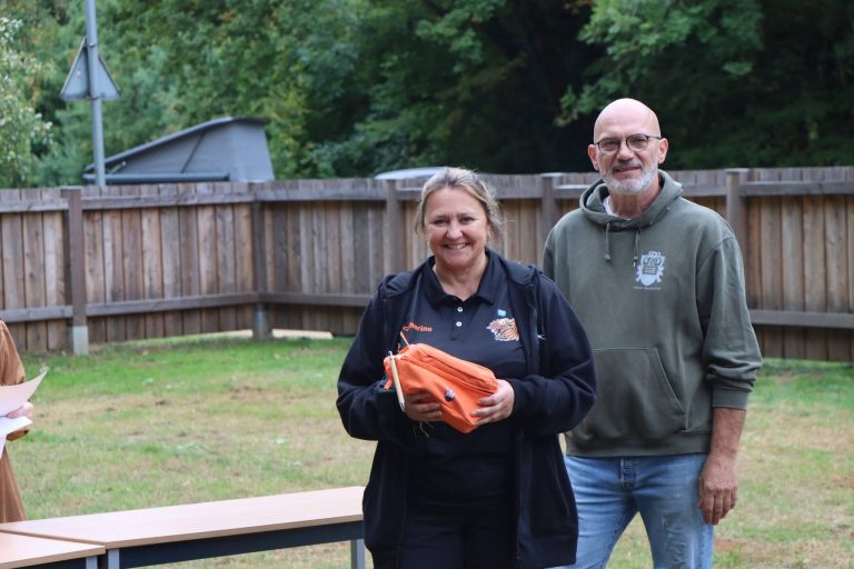 Lächelnde Frau mit orangefarbenem Preis neben einem Mann im grauen Pullover