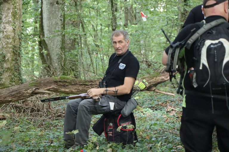 Bogenschütze mit Bogen sitzt auf einem Hocker im Wald und wartet