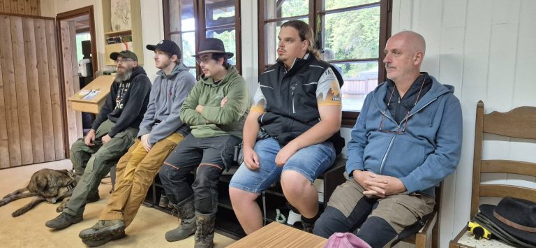 Fünf Männer sitzen nebeneinander auf einer Bank im Vereinshaus