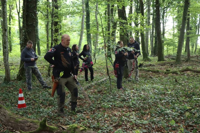 Bogenschützengruppe an einer Station im Wald, rot-weißer Leitkegel am Rand