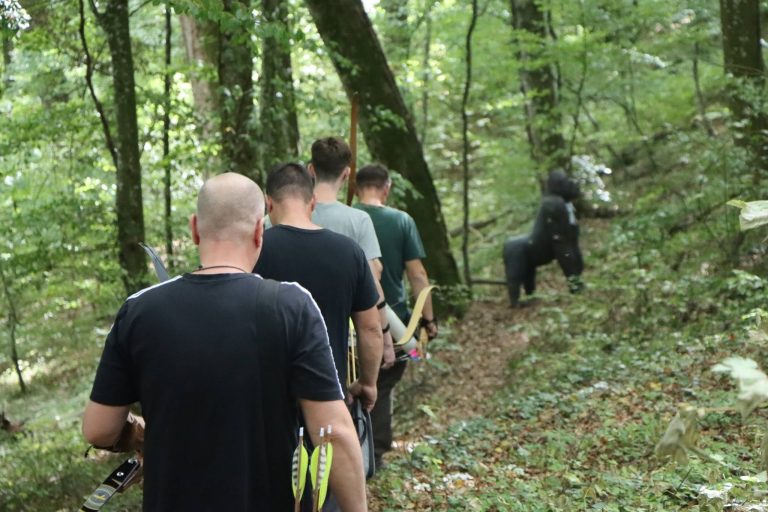 Bogenschützen gehen hintereinander einen Waldpfad entlang zur nächsten Station