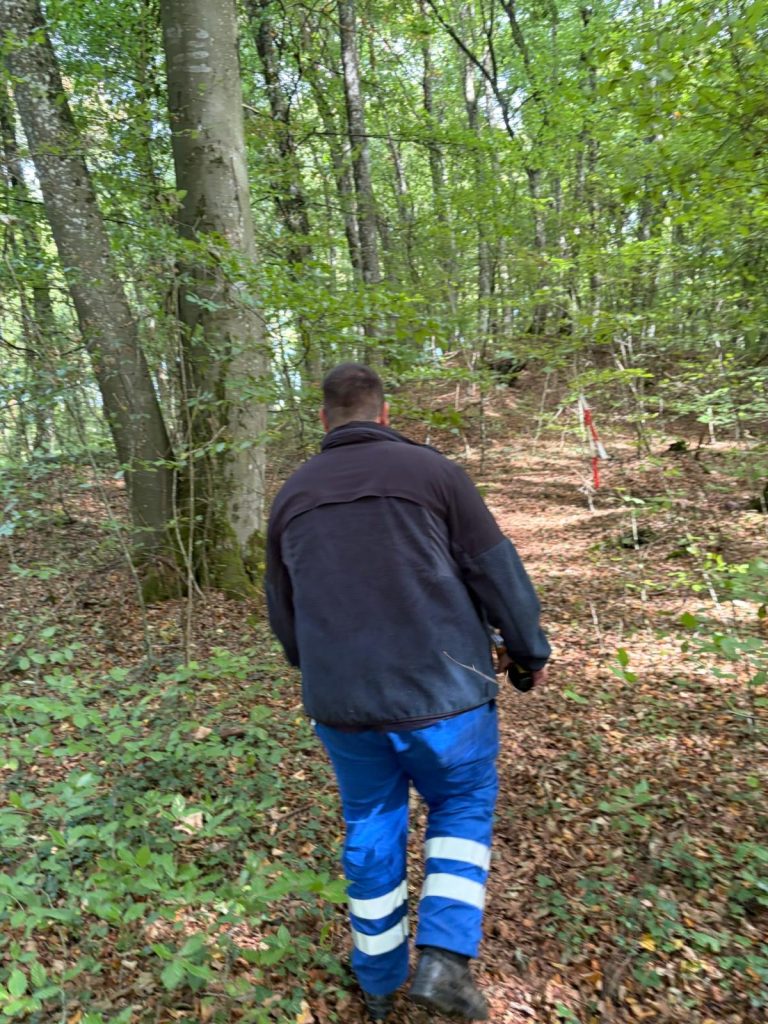 Mann in dunkler Jacke und blauer Arbeitshose geht in den Wald hinein
