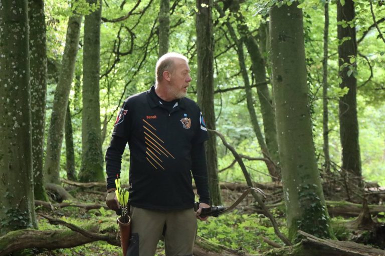Bogenschütze in schwarzer Jacke steht mit seinem Bogen im Wald