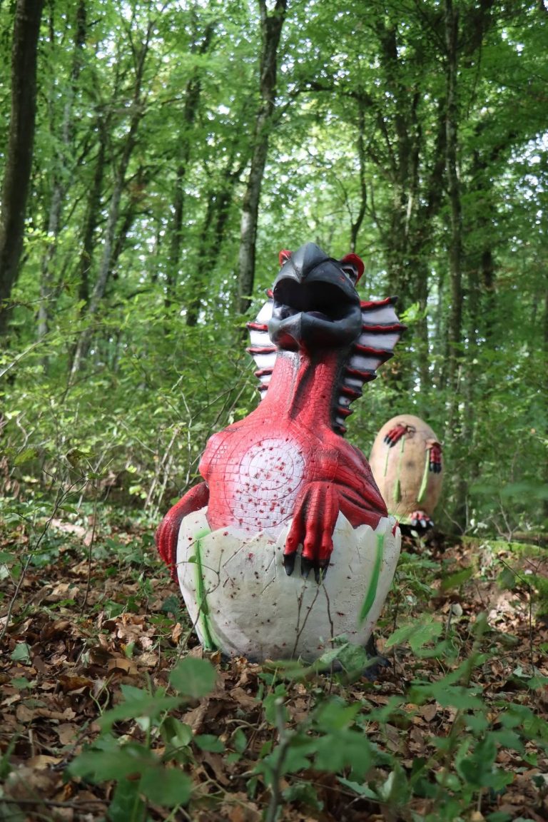 3D-Ziel eines rot-weißen Dinosaurierbabys, das aus einem Ei schlüpft, im Waldlaub
