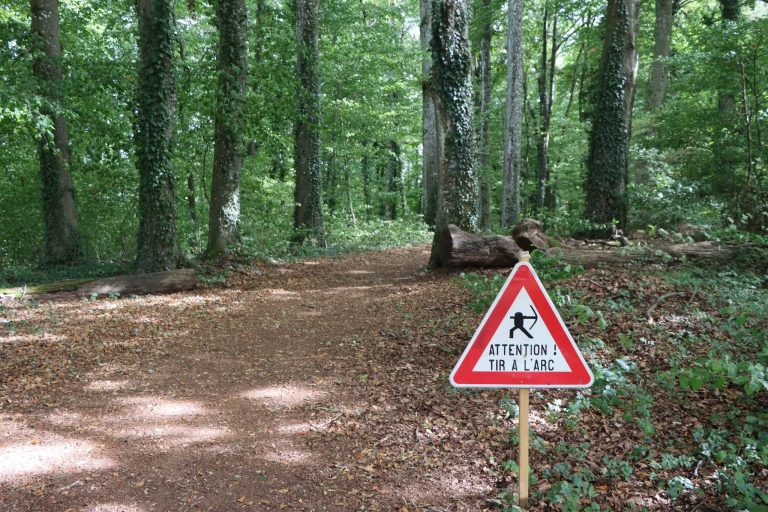 Dreieckiges Warnschild „Attention tir à l'arc“ am Waldweg