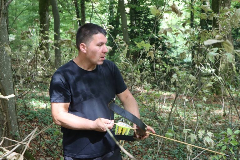 Bogenschütze in schwarzem T-Shirt legt im Wald einen Pfeil auf den Bogen