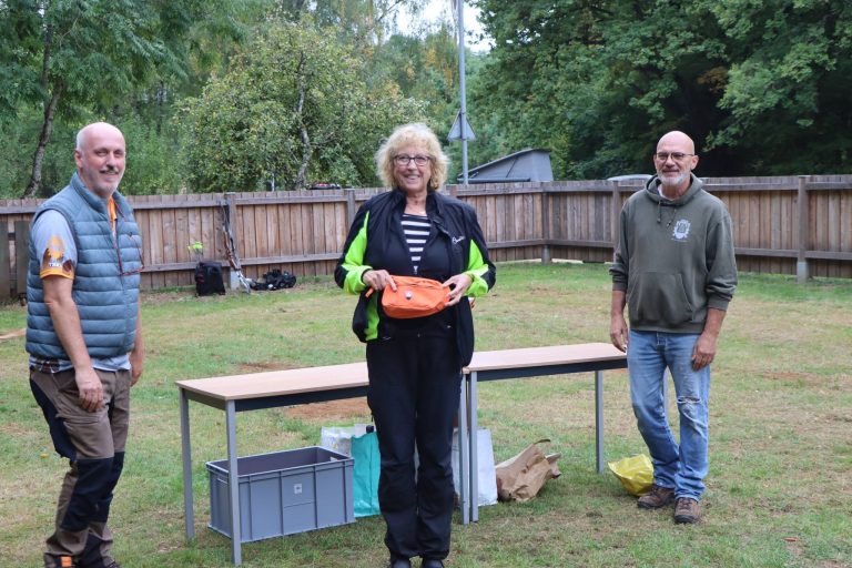 Frau mit orangefarbenem Preis zwischen zwei Männern bei der Siegerehrung