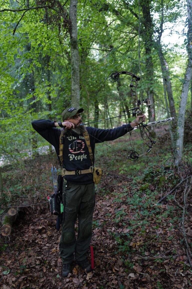 Bogenschütze in dunkler Kleidung spannt den Bogen am Waldhang