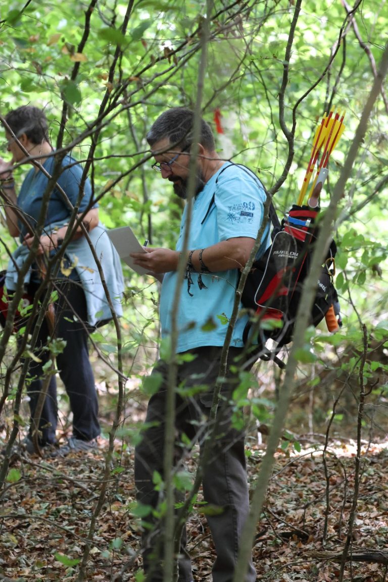 Zwei Bogenschützen mit Köcher tragen im Wald die Punkte auf der Wertungskarte ein